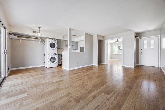 unfurnished living room featuring light wood-type flooring, visible vents, stacked washer and clothes dryer, baseboards, and ceiling fan