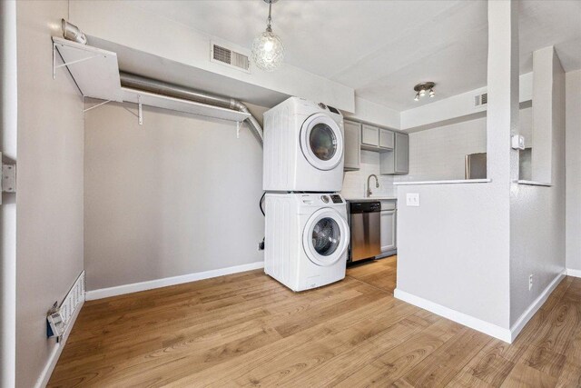 washroom featuring visible vents, stacked washer / drying machine, and light wood finished floors