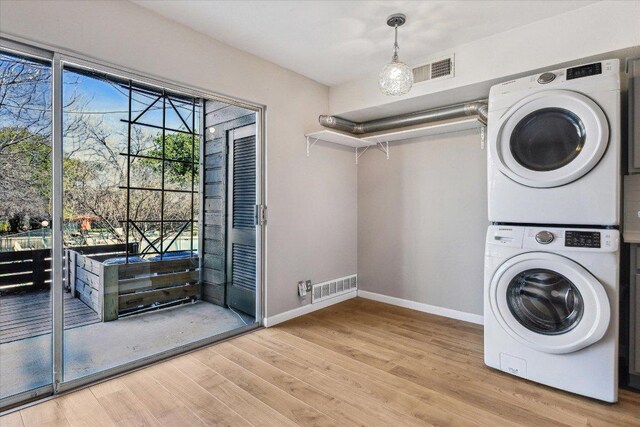 laundry room featuring stacked washer / dryer, baseboards, visible vents, and wood finished floors