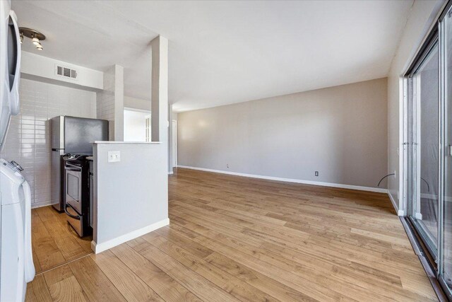 kitchen with baseboards, visible vents, light wood-style flooring, electric stove, and stacked washer / drying machine