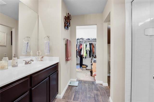 bathroom featuring baseboards, tiled shower, wood finished floors, and vanity