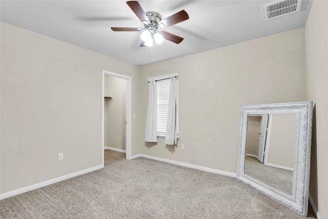 unfurnished bedroom with a spacious closet, visible vents, baseboards, carpet floors, and a ceiling fan