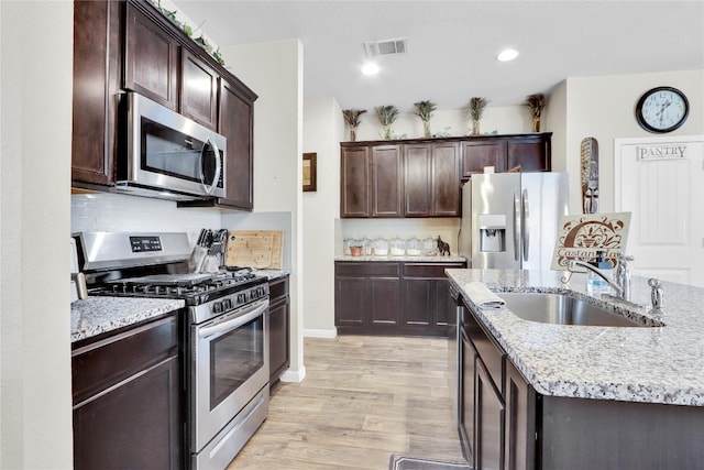 kitchen featuring light wood finished floors, visible vents, light stone countertops, appliances with stainless steel finishes, and a sink