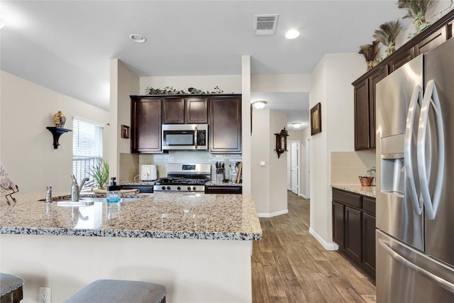 kitchen featuring visible vents, light stone countertops, dark brown cabinetry, and appliances with stainless steel finishes