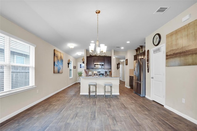 kitchen with dark wood-style floors, baseboards, stainless steel appliances, dark brown cabinets, and a kitchen bar