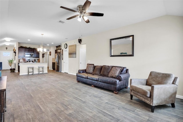 living room featuring visible vents, ceiling fan with notable chandelier, wood finished floors, baseboards, and vaulted ceiling