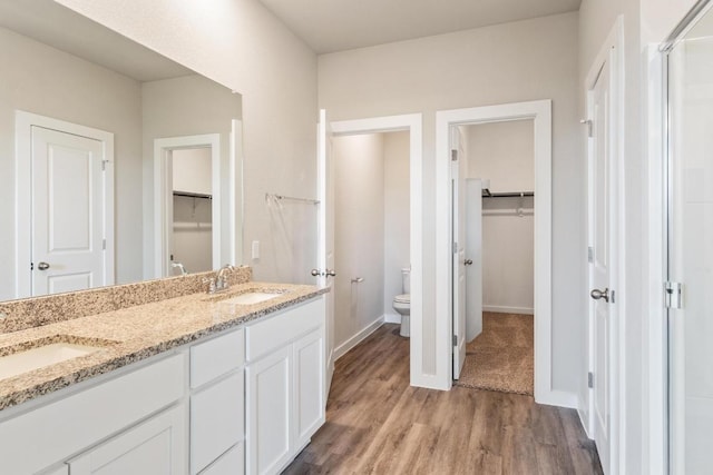 full bath with wood finished floors, toilet, a walk in closet, and a sink