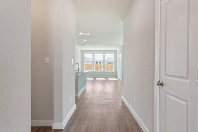 hallway featuring visible vents, baseboards, and wood finished floors