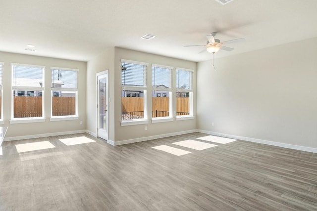 unfurnished room with a ceiling fan, wood finished floors, visible vents, and baseboards