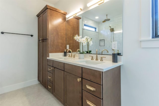 full bath featuring double vanity, baseboards, a tile shower, and a sink