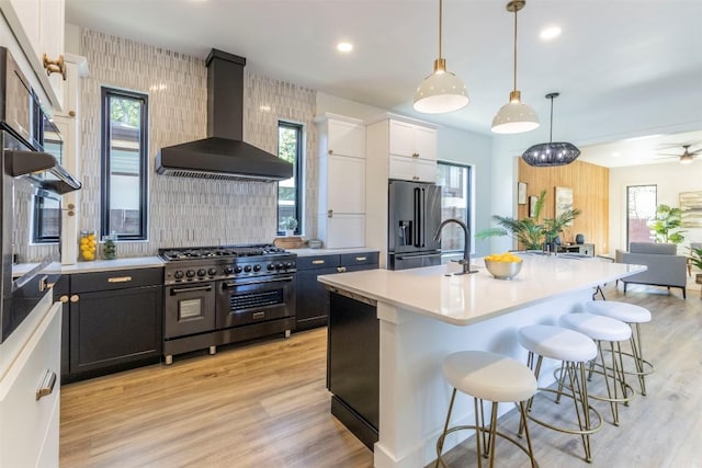 kitchen with light countertops, wall chimney range hood, high end appliances, and light wood-style flooring