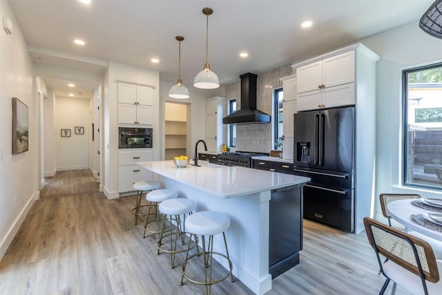 kitchen featuring light wood-style flooring, black appliances, a kitchen breakfast bar, exhaust hood, and tasteful backsplash