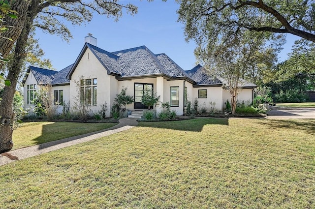 french country inspired facade with stucco siding, a chimney, and a front lawn