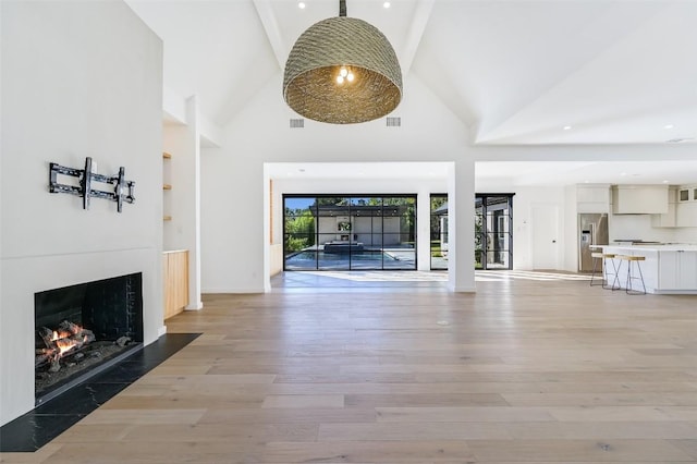 unfurnished living room with a fireplace with flush hearth, light wood-style flooring, and high vaulted ceiling