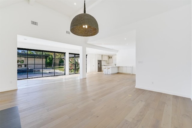 unfurnished living room with visible vents, baseboards, high vaulted ceiling, and light wood-style flooring