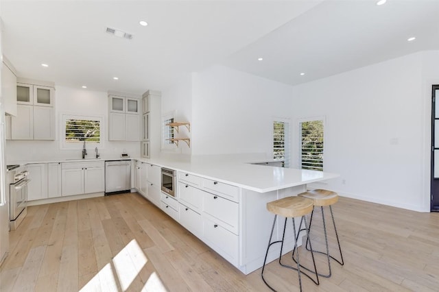 kitchen featuring visible vents, light wood finished floors, a peninsula, a sink, and appliances with stainless steel finishes