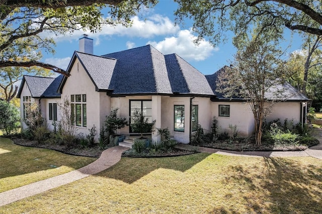 view of front of home with stucco siding, a chimney, a front lawn, and roof with shingles