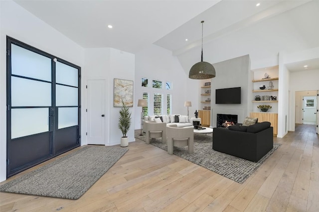 living room featuring recessed lighting, light wood-style floors, a lit fireplace, and high vaulted ceiling