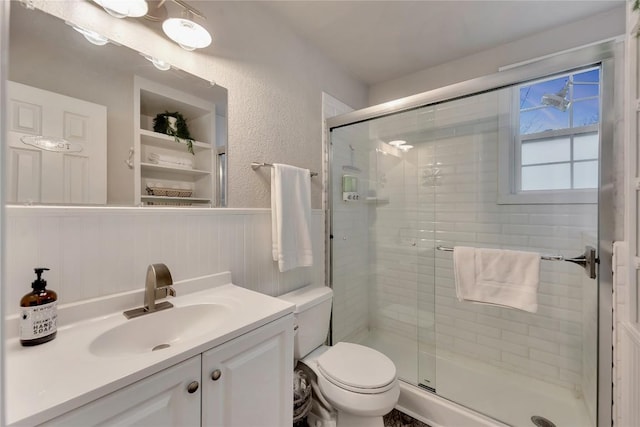 bathroom featuring toilet, a stall shower, vanity, and a textured wall