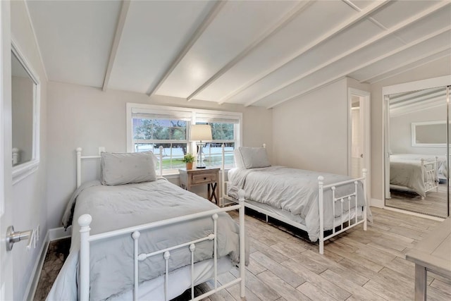 bedroom featuring light wood finished floors, vaulted ceiling with beams, and baseboards