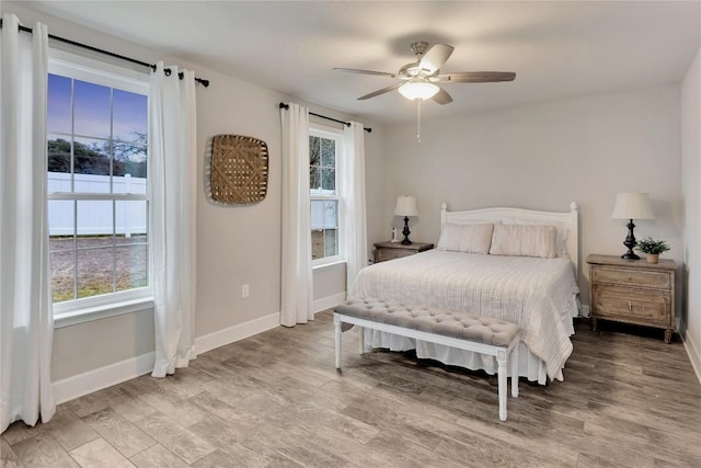 bedroom featuring multiple windows, light wood-style flooring, baseboards, and ceiling fan