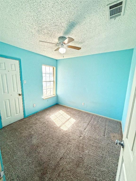 carpeted spare room with visible vents, a textured ceiling, and a ceiling fan