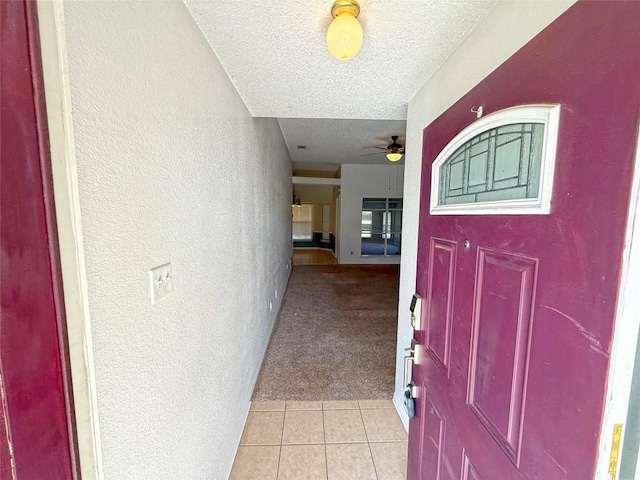 foyer with ceiling fan, light colored carpet, light tile patterned floors, a textured wall, and a textured ceiling