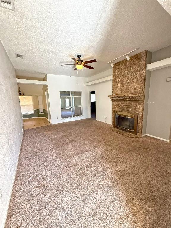 unfurnished living room featuring a ceiling fan, a fireplace, visible vents, and carpet floors