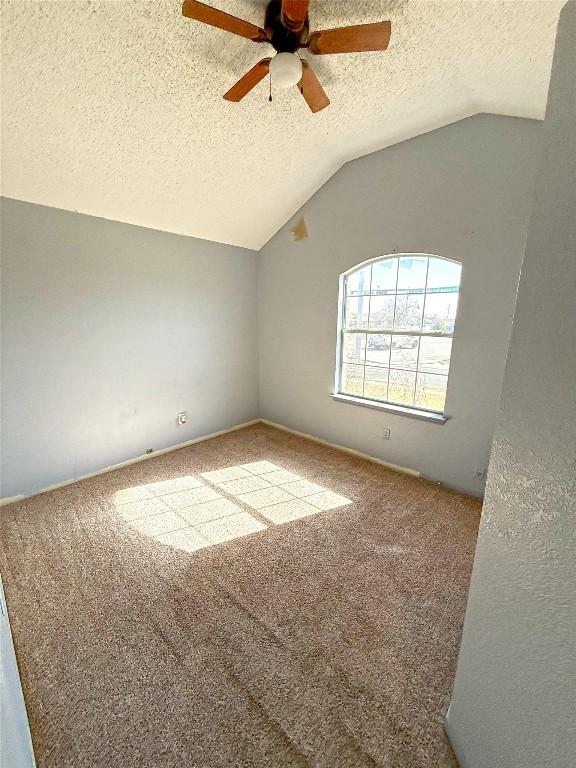 unfurnished room featuring carpet flooring, a textured ceiling, lofted ceiling, and a ceiling fan