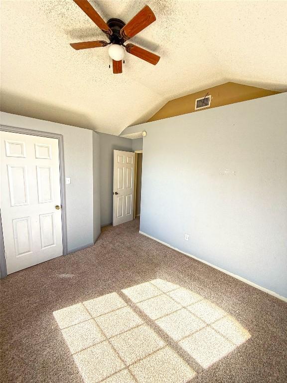 unfurnished bedroom with carpet flooring, visible vents, a textured ceiling, and lofted ceiling