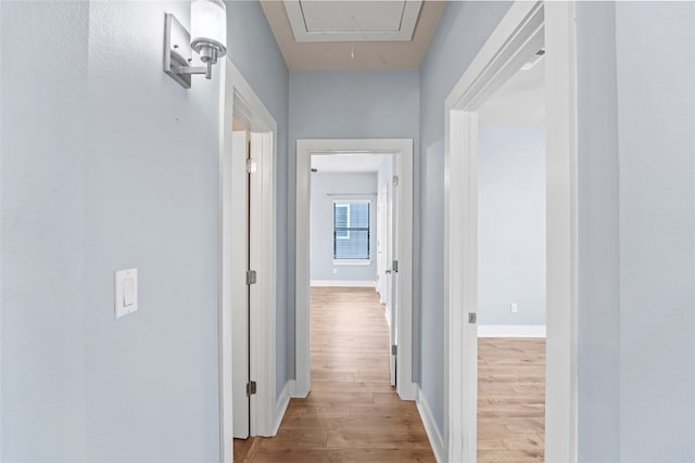 hall featuring baseboards, attic access, and wood finished floors