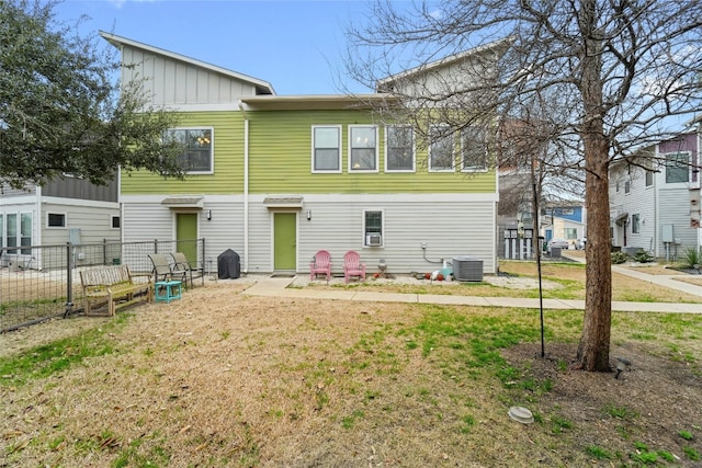 rear view of property with central air condition unit, a yard, board and batten siding, and fence