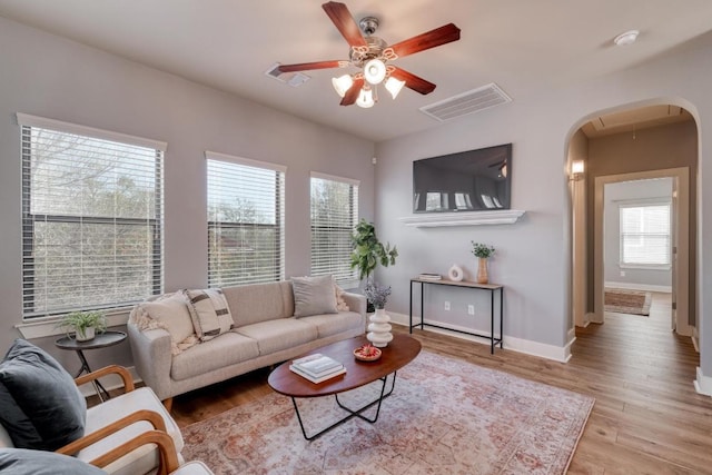 living area with visible vents, baseboards, attic access, wood finished floors, and arched walkways