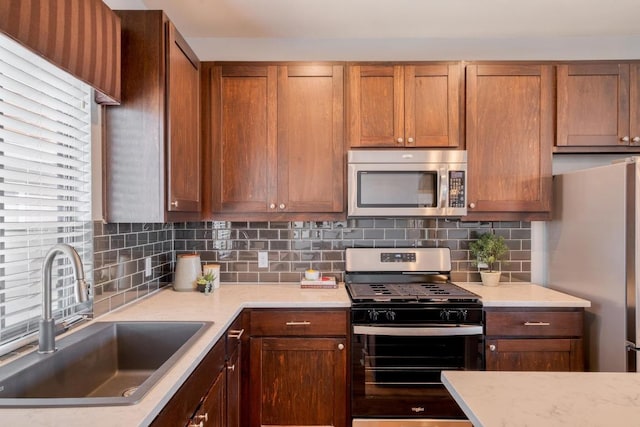 kitchen with brown cabinetry, backsplash, appliances with stainless steel finishes, and a sink