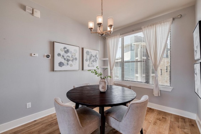 dining space featuring light wood-style flooring, a notable chandelier, and baseboards