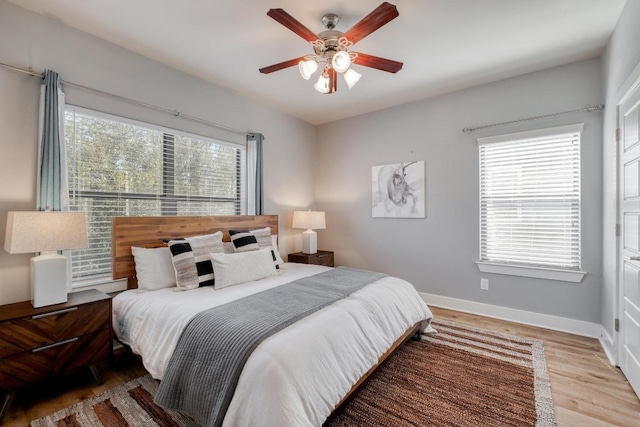 bedroom featuring a ceiling fan, multiple windows, wood finished floors, and baseboards