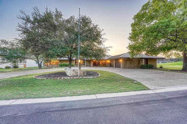 view of front of house featuring an attached garage, a lawn, and curved driveway