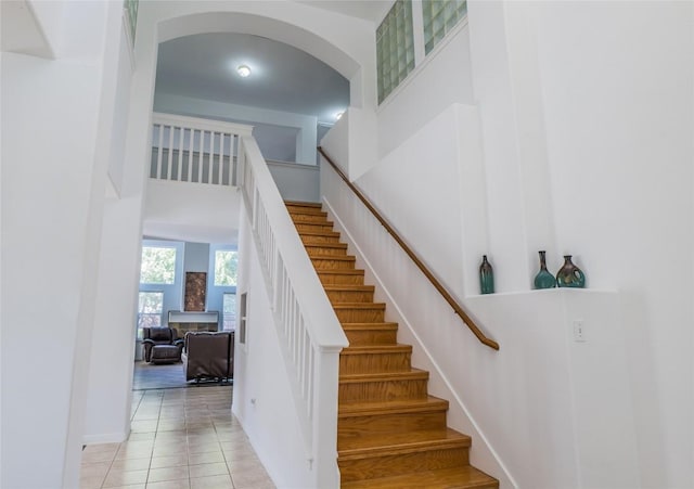 stairway featuring tile patterned floors, arched walkways, a fireplace, and a towering ceiling