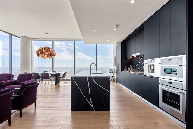 kitchen with expansive windows, modern cabinets, dark cabinets, and light wood finished floors