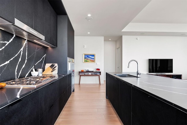 kitchen with a sink, light wood-style flooring, modern cabinets, and dark cabinets