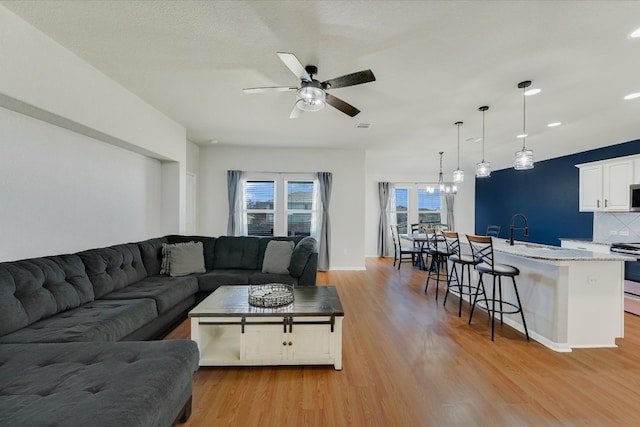 living area with light wood-style flooring, recessed lighting, ceiling fan with notable chandelier, and baseboards