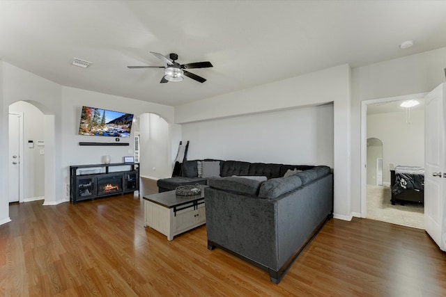 living area featuring arched walkways, a fireplace, a ceiling fan, and wood finished floors