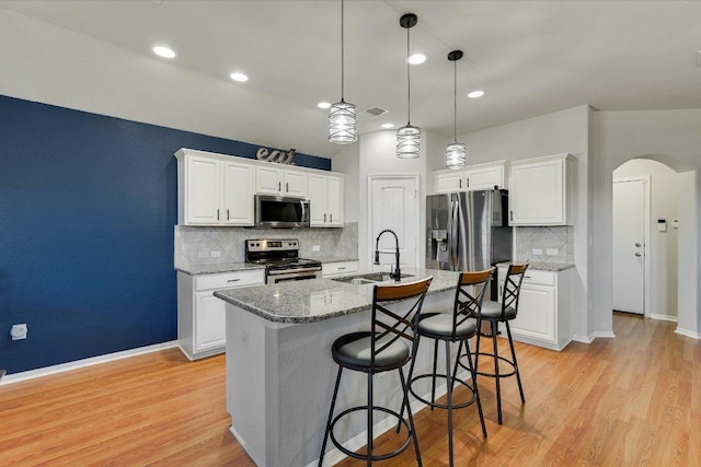 kitchen featuring light wood-type flooring, an island with sink, appliances with stainless steel finishes, arched walkways, and a sink