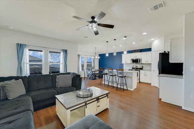 living area with ceiling fan with notable chandelier, recessed lighting, wood finished floors, and visible vents