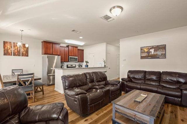 living area featuring visible vents, a chandelier, and light wood finished floors