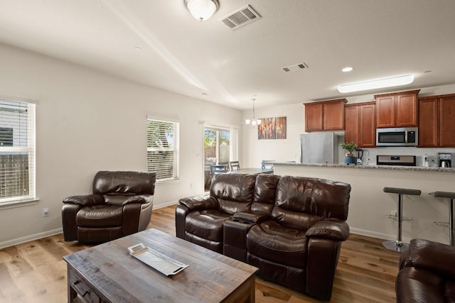 living area featuring visible vents, light wood-style floors, and a notable chandelier