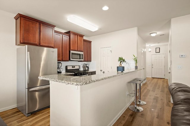 kitchen featuring tasteful backsplash, a kitchen bar, light stone counters, appliances with stainless steel finishes, and light wood-style floors