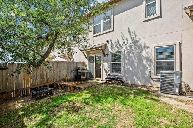 rear view of house with stucco siding, a yard, central AC, and fence