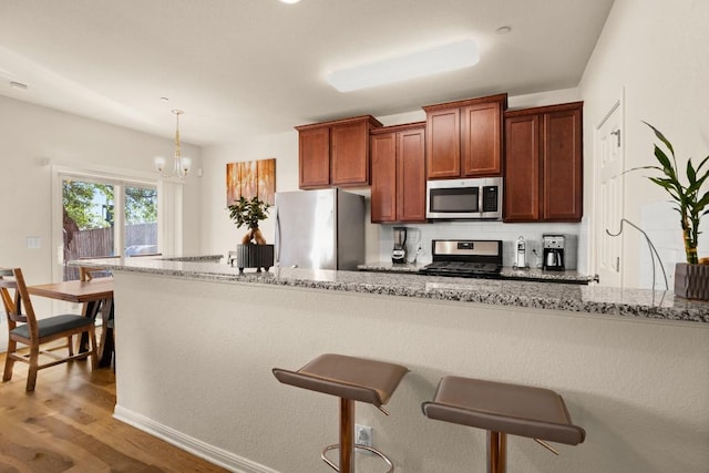 kitchen with light stone counters, stainless steel appliances, a kitchen breakfast bar, and wood finished floors