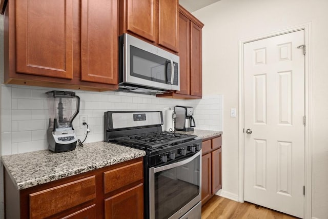 kitchen featuring light stone counters, stainless steel appliances, decorative backsplash, light wood-style floors, and brown cabinets